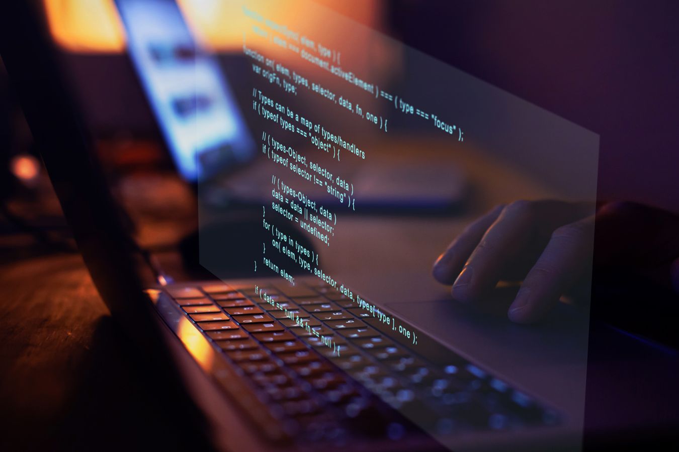 A person coding on a laptop in a dimly lit room, working on IT consulting.