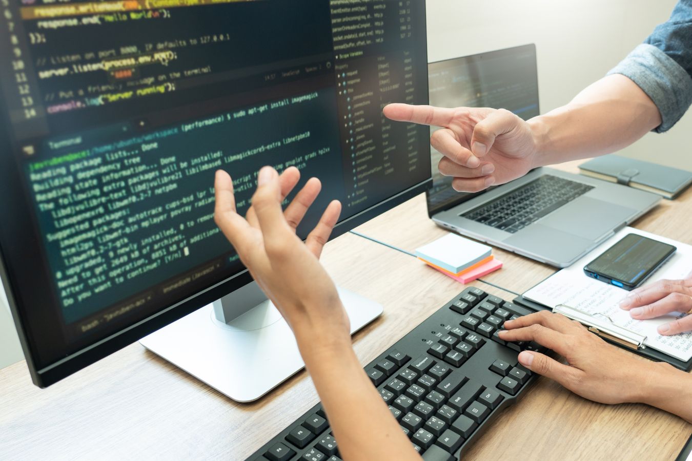 Two individuals engaging in technology consulting while collaborating on software development in front of computer screens with code visible on the monitor.