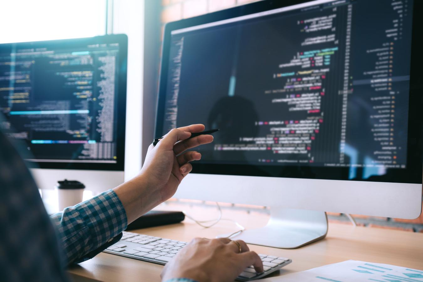 Programmer working on code at a dual-monitor workstation, specializing in Managed Security Services.