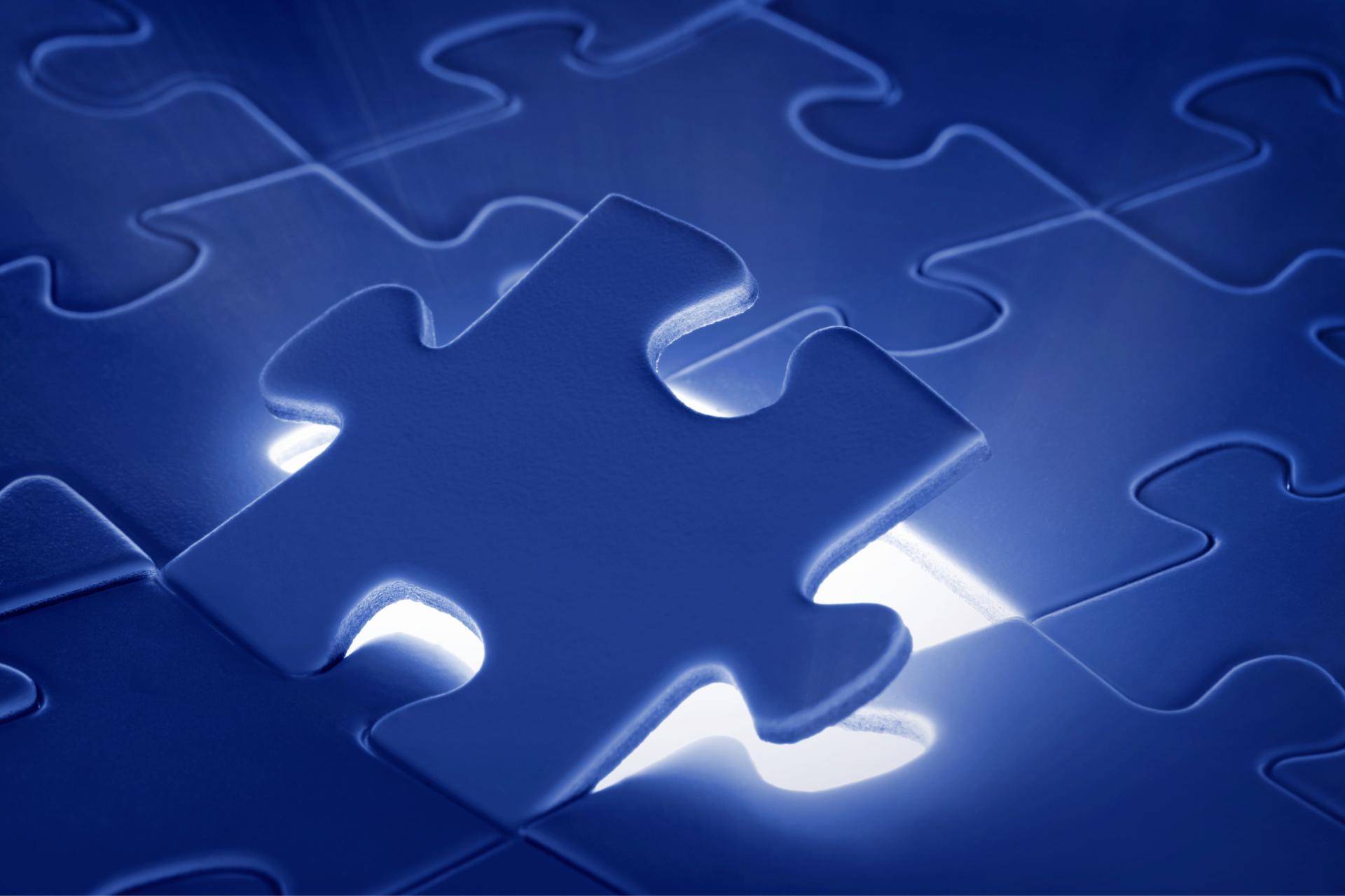 A single puzzle piece stands above a nearly complete jigsaw puzzle, illuminated by light from below. Thank you.