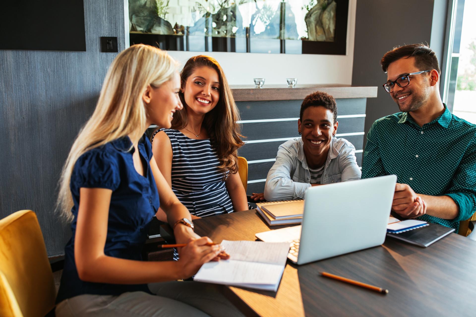 Four colleagues in a meeting discussing work with a laptop and reading it blog articles on the table. "Thank you," one of them says after a helpful suggestion.