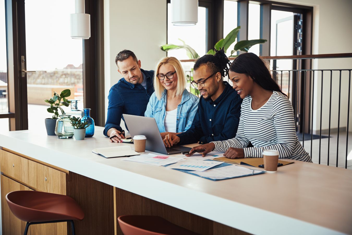 Four colleagues using a laptop and discussing staffing and recruiting work in a modern office setting.