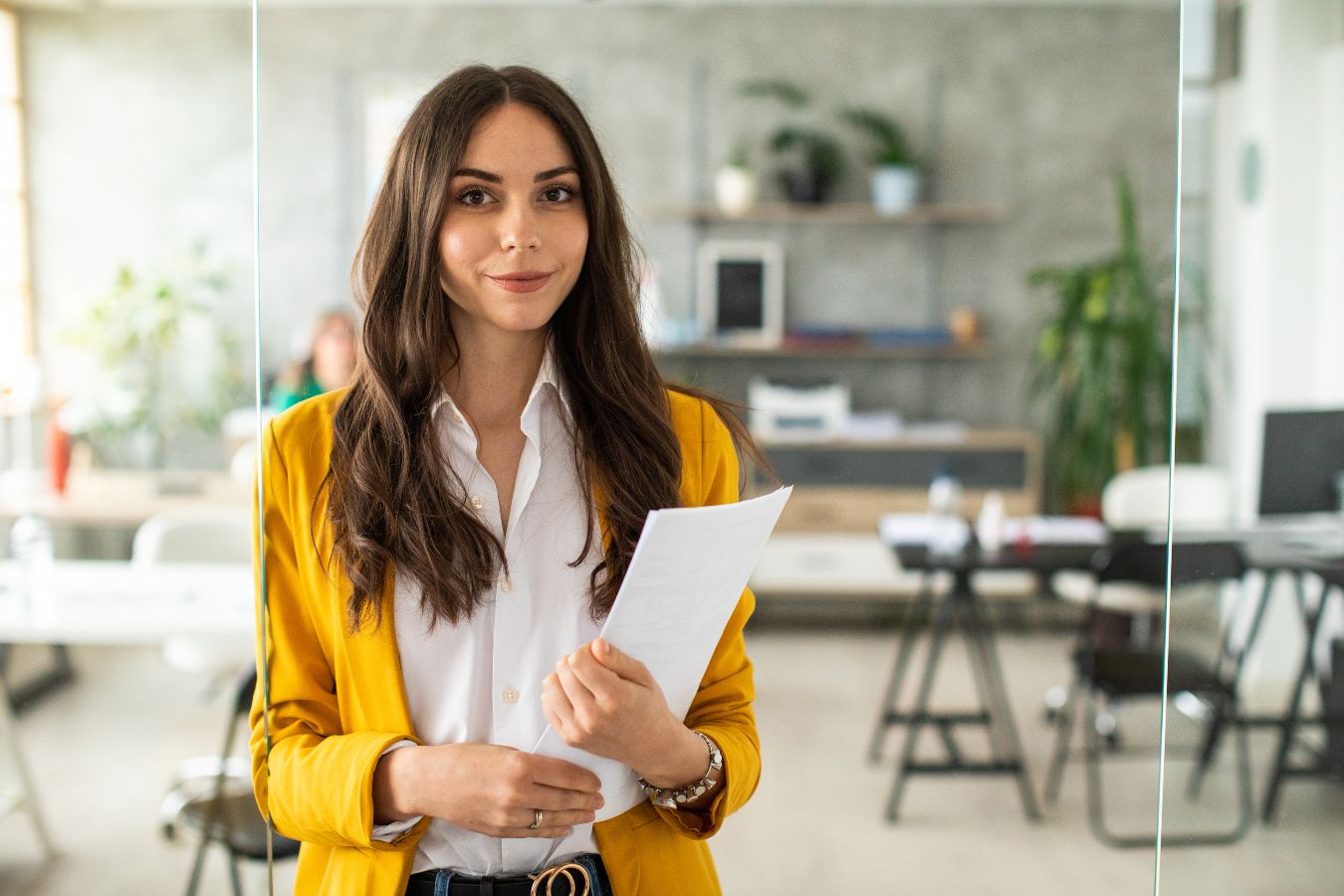 Professional woman in a yellow blazer holding documents related to Talent Acquisition in an office environment.