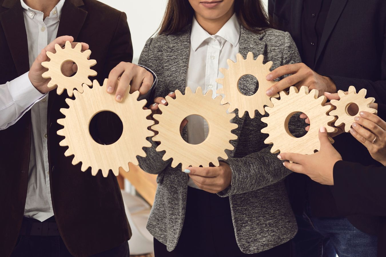 Team members holding interlocking wooden gears together, symbolizing the recruiting efforts of staffing agencies.