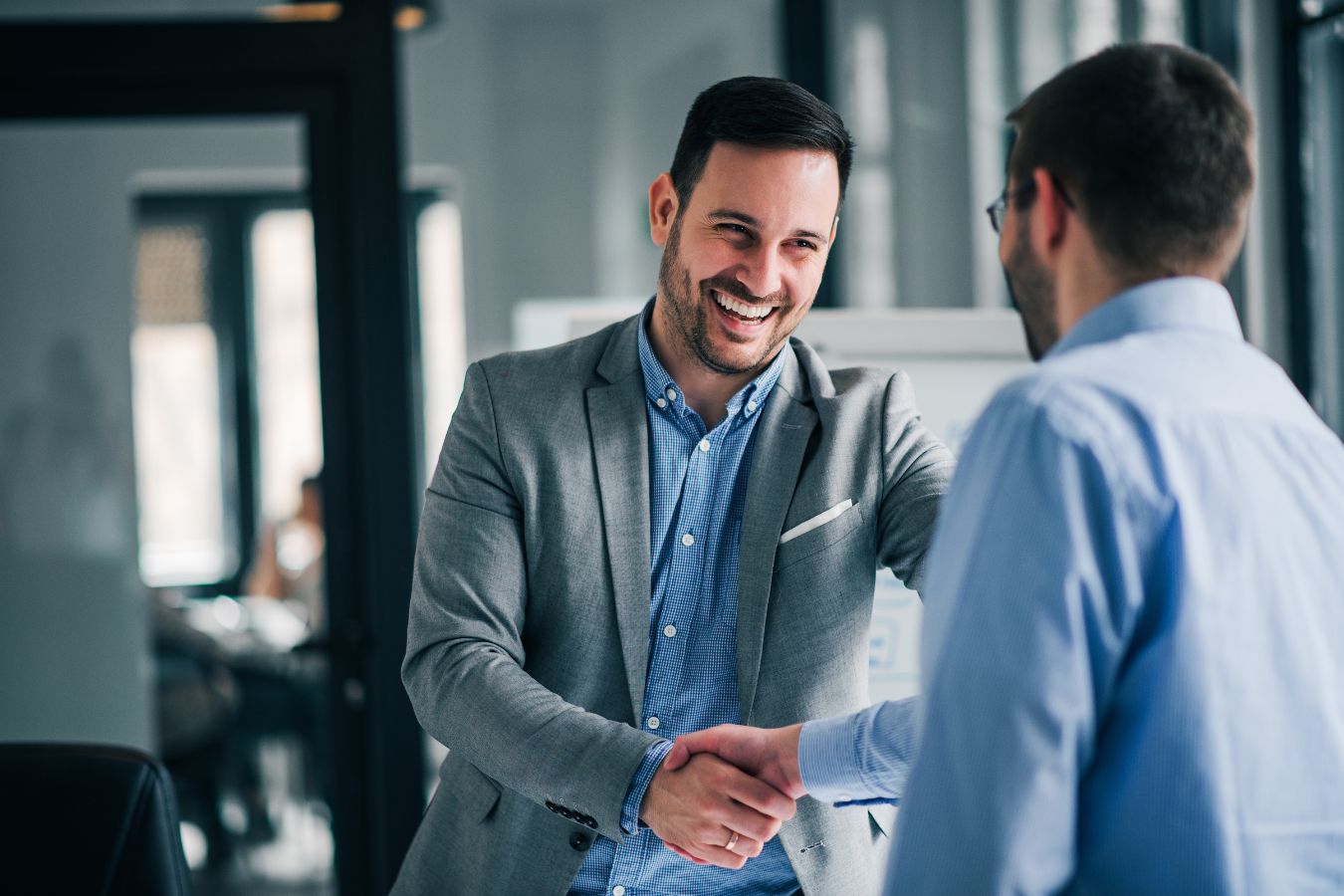 Two professionals shaking hands and smiling in a staffing and recruiting office environment.