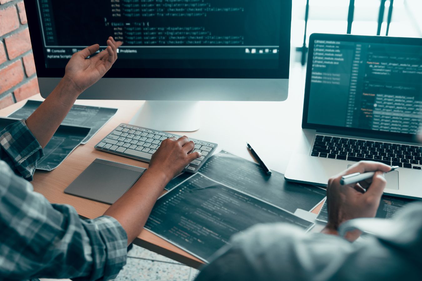 Software development programmer working on code at a dual-monitor workstation.