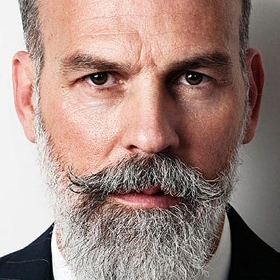 Close-up of a mature man with a full beard and mustache, wearing a suit.