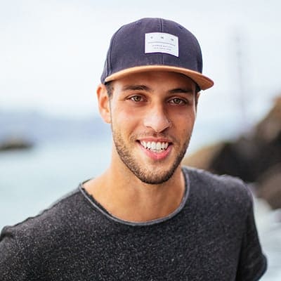 A smiling young man wearing a baseball cap outdoors.